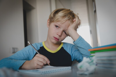 Photograph of primary-age boy struggling with maths homework and looking despondent.